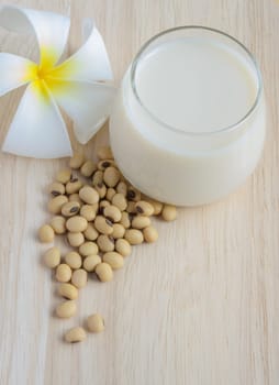 Fresh Soy milk (Soya milk) and dried soybean seeds on wooden background with white plumeria flower. Traditional staple of East Asian cuisine