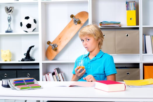 blond boy doing homework and drinking juice