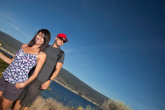 Outdoor photo of young, attractive couple hiking with mountains and lake in background.