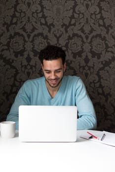 Young man using a laptop at home. He is looking at the screen and smiling.