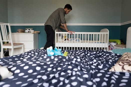 Young father checking on his baby son, who is asleep in a copt in the bedroom.