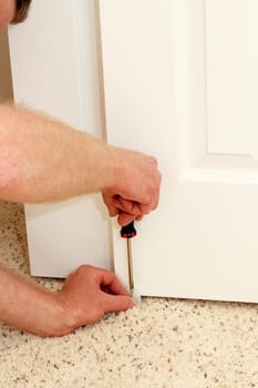 Caucasian male using a screwdriver to screw in a bypass door guide at the bottom middle carpeted floor of a home closet door. Installing a white plastic door guide.