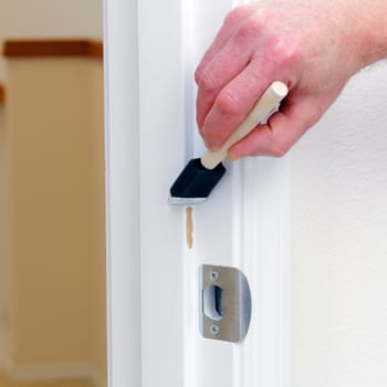 Hand of a man painting a door frame with touch-up paint that had some paint scraped off. Fixing up a home with touch up paint in order to help sell a home.
