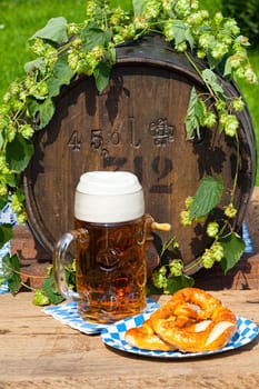 Beer barrel with hops, a large glass of beer and a pretzel on a paper plate