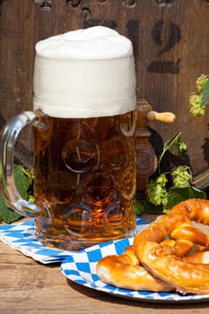 Beer barrel with hops, a large glass of beer and a pretzel on a paper plate