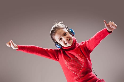 Little girl listening to the music, dancing and showing thumbs up happily