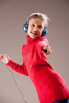 Little girl dancing and pointing her finger to you while listening to the music in her blue headphones and dancing