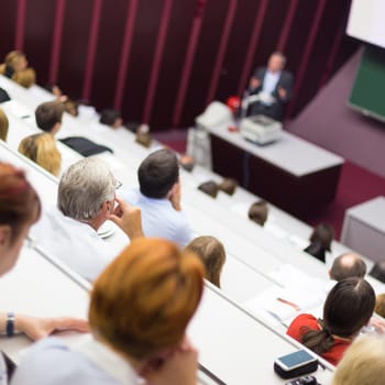 Lecturer at university. Healthcare expert giving a talk to medical faculty professors. Participants listening to lecture and making notes.