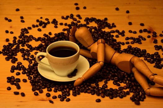 Cup of coffee on wooden table with coffee beans and wooden figure is next to it