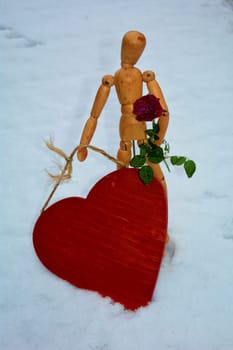 HOLZPUPPE STEHT WITH ROTEM HOLZHERZ AND ROTER ROSE IN WHITE SCHNEE