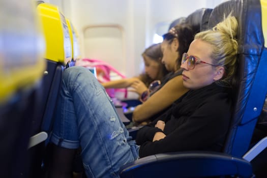 People flying by plane. Interior of airplane with passengers sleeping on seats. Tired woman napping on uncomfortable seat on airplane. Commercial transportation by planes.