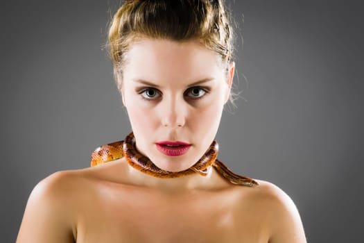 A pretty young woman with brunette hair looks at the camera head to her bare neck snaking a red snake.