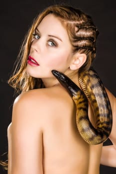 Beautiful brunette young woman with a snake (python) has swung around her neck. She looks at us over his shoulder