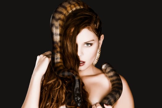 A pretty young woman with brunette hair looks at the camera head to her bare neck snaking a big dark snake.