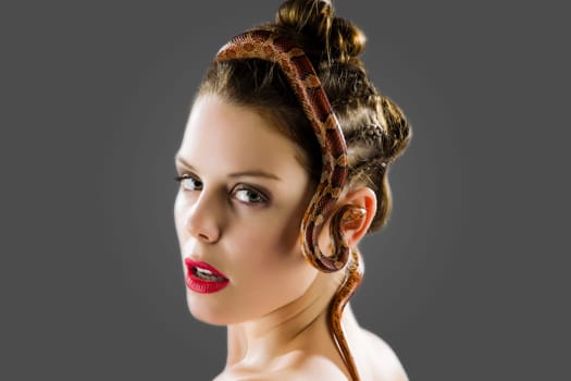 A pretty young woman with brunette hair looking over her bare shoulder at the camera in her hair sitting a red natter the curls over her ear