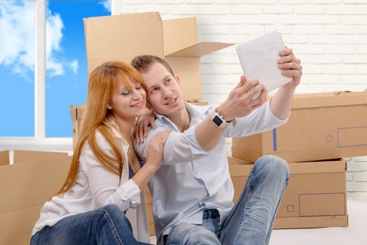 a happy couple sitting on the floor taking selfie in their new house