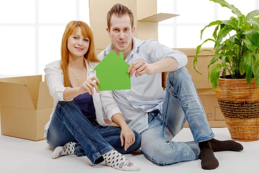 smiling young couple sitting after moving house, holding green house model