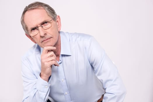 Senior man looking at camera seriously with hand on chin