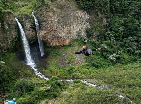Tourist gliding on the zip line trip against Bridal veil (Manto de la novia), waterfall in Cascades route, Banos, Ecuador