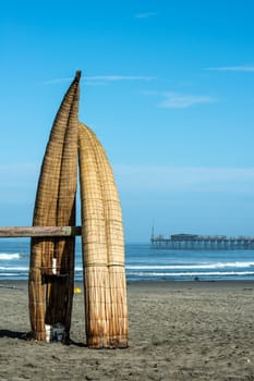 Traditional Peruvian small Reed Boats (Caballitos de Totora), straw boats still used by local fishermens in Peru. On the background – Famous pier at Pimentel