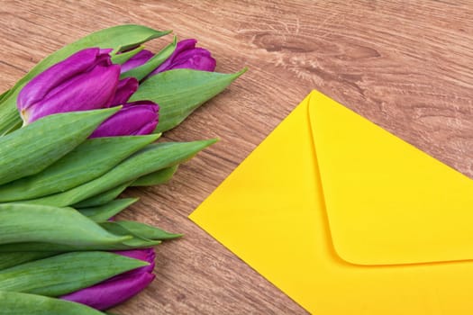Yellow envelope with purple tulips on a wooden background