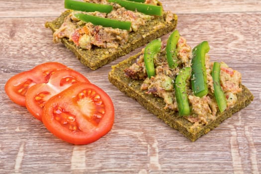 Raw bread with a spread decorated with green pepper and tomatoes