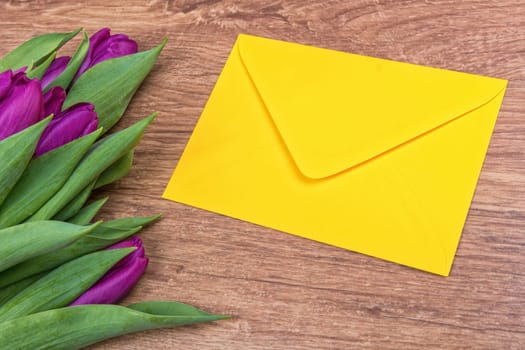 Yellow envelope with purple tulips on a wooden background