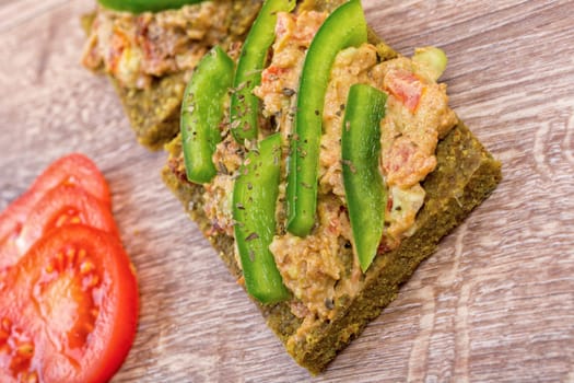 Raw bread with a spread decorated with green pepper and tomatoes