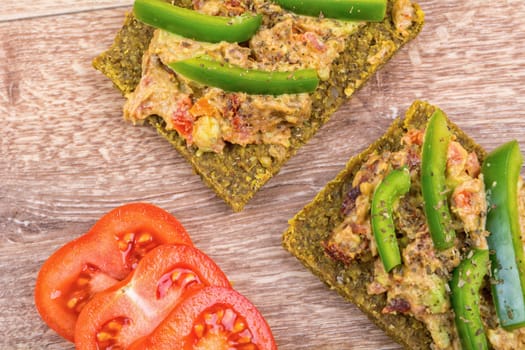 Raw bread with a spread decorated with green pepper and tomatoes