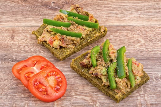 Raw bread with a spread decorated with green pepper and tomatoes
