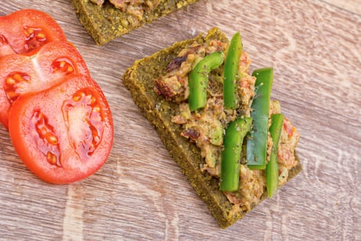 Raw bread with a spread decorated with green pepper and tomatoes
