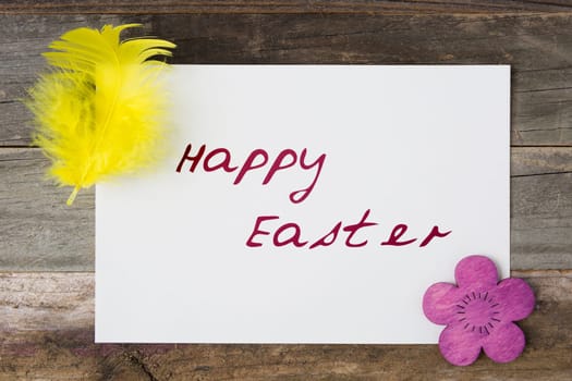 Happy Easter greeting card surrounded by feather and wooden Easter flower.