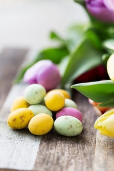 Close up of milk chocolate eggs on table with flowers vertical orientation.