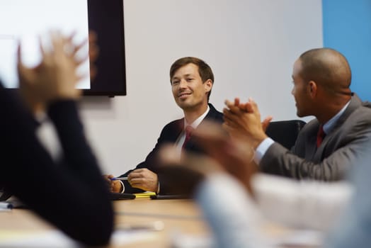 Group of business people meeting in corporate conference room, applauding at a coworker during his presentation. The man is showing charts and slides on a big TV monitor