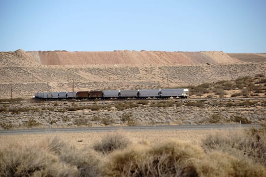 A freight train crosses the Mojave Desert with piled up sand slopes.