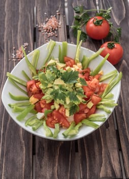 Fresh salad with avocado,tomatoes,lgreen paper and spices on wooden board