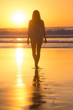 Woman walking on sandy beach in sunset leaving footprints in the sand. Beach, travel, concept. Copy space. Vertical composition.