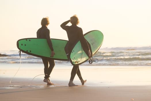 Male surfers on sandy beach with the surfboard in sunset.