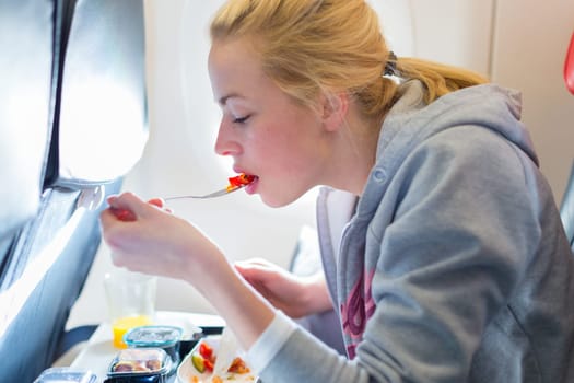 Woman eating meal on commercial airplane.