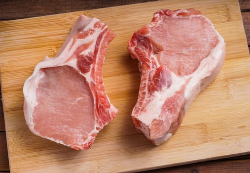 Raw Pork chops, lying on a wood board ready for cooking