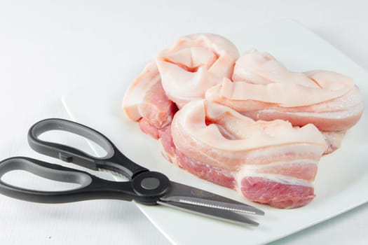 streaky pork with scissors in plate on white background