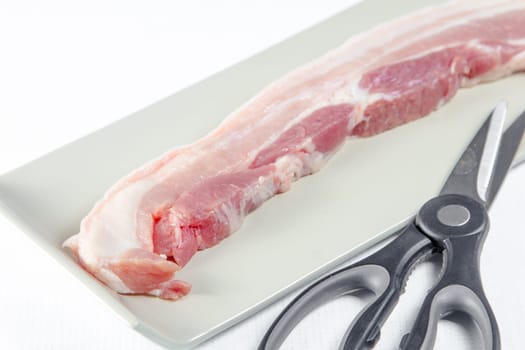 streaky pork with scissors in plate on white background