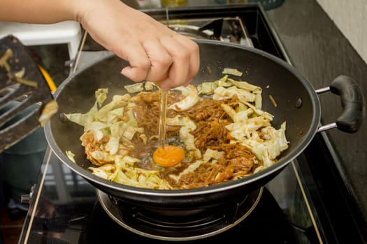 chef cracking an egg into fried noodle in pan for thai food menu