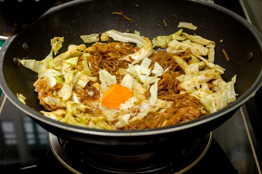 chef cracking an egg into fried noodle in pan for thai food menu