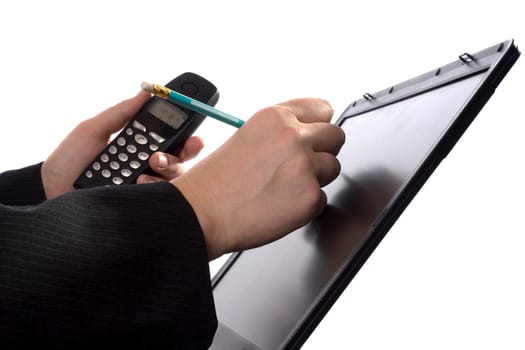 A businessman is writing notes in his agenda on a laptopscreen while holding a mobile phone.