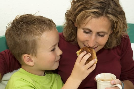 Boy giving his mommy a bite of his raisin bun.