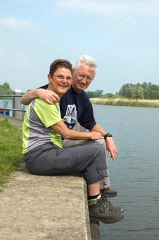 Happy senior couple relaxing and enjoying the sun, sitting at the harbour
