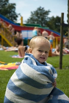 Boy in a towel warming up after swimming in a pool.