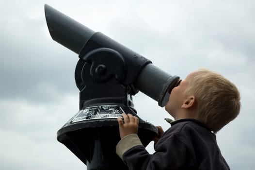 Boy looking into the sky through a telescope.