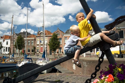 Two boys on an anchor, in front of a beautiful harbor.